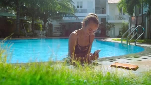 Menina com corpo na água da piscina lê sms no telefone na barreira — Vídeo de Stock