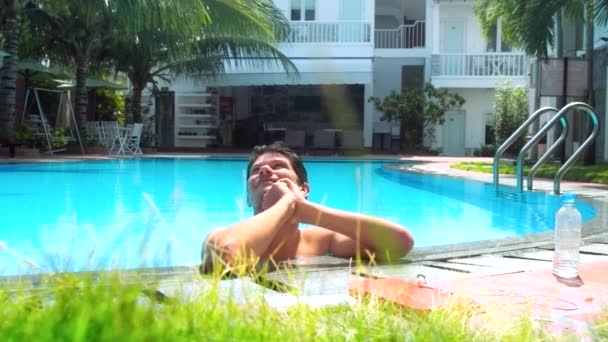 Tipo se para en el agua azul en la barrera de la piscina mira hacia arriba — Vídeos de Stock