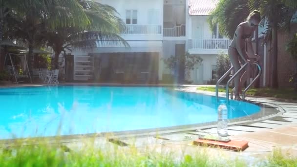 Спортивная девушка в бикини спускается к бассейну по металлической лестнице — стоковое видео