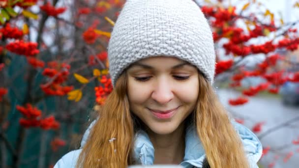 Blond fille en tricot chapeau surf internet à rouge rowan arbre — Video