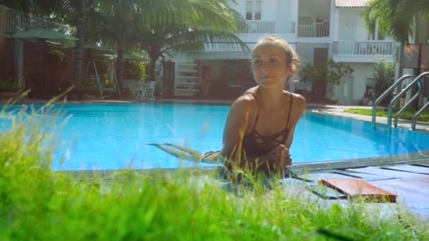 Mignonne fille blonde en bikini repose dans la piscine appuyé sur la barrière — Video