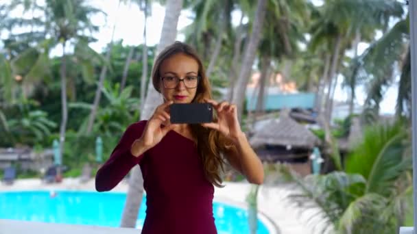 Довгошерста дівчина в окулярах фотографії проти басейну долонями — стокове відео
