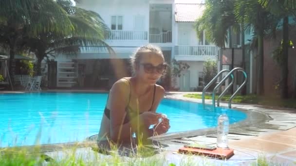 Jolie fille met écouteur dans oreille appuyé sur la barrière de la piscine — Video