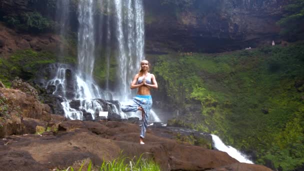 Menina segura pose na perna dobra palmas no peito na cachoeira — Vídeo de Stock