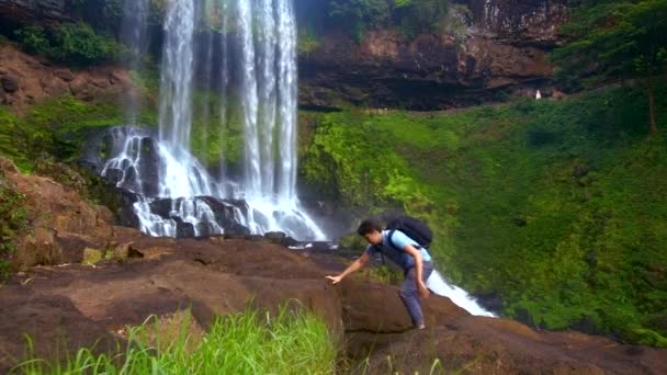赤脚男子背包爬上岩石在瀑布 — 图库视频影像