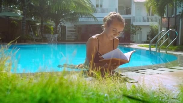 Chica con cuerpo en piscina agua mira a través de libro en la barrera — Vídeos de Stock