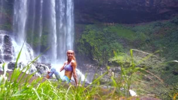 Hübsches Mädchen ruht sich gegen Wasserfall hinter Gras aus — Stockvideo