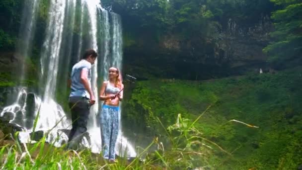 Mann kommt zu Mädchen Umarmungen an der Taille macht Selfie am Wasserfall — Stockvideo