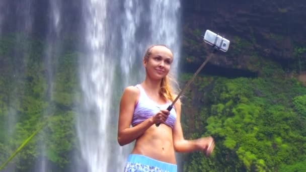 Girl with ponytail makes selfie against beautiful waterfall — Stock Video