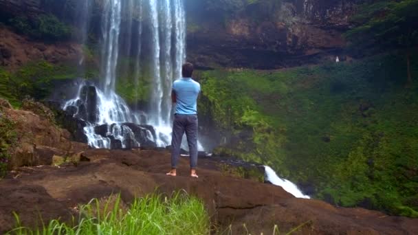 Hintermann steht auf Felsen und beobachtet mächtigen Wasserfall — Stockvideo