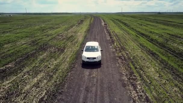 Белый автомобиль едет по наземной дороге среди обширных полей — стоковое видео