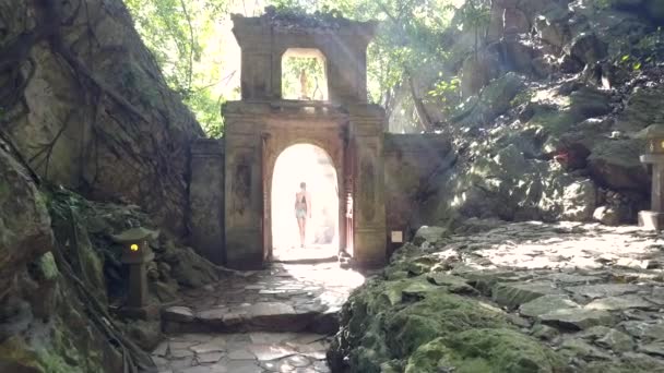 Mujer vista trasera camina a través de la puerta en arco de piedra — Vídeo de stock