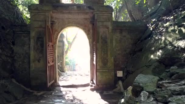 Girl tourist approaches cave stone arch against sunlight — Stock Video