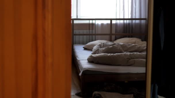 Man achter bruine gordijnen maakt tweepersoonsbed tegen raam — Stockvideo