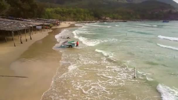 Waves roll on beach up to awnings people move scooter — Stock Video