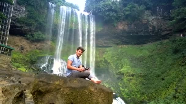 Killen sitter på sten med drönare fjärrkontroll av vattenfall — Stockvideo