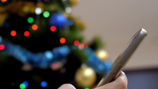 बंद धीमी गति लड़की क्रिसमस पेड़ पर फोन पर एसएमएस पढ़ती है — स्टॉक वीडियो