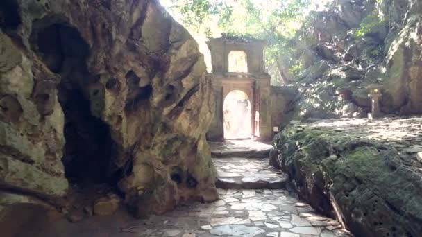 Mulher distante entra caverna através de arco de pedra contra a luz — Vídeo de Stock