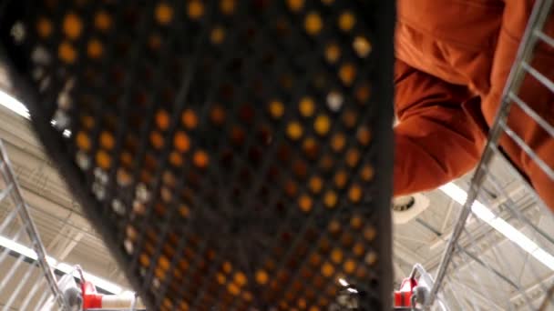Mann in roter Jacke steckt orangefarbene Schachtel in Einkaufswagen — Stockvideo