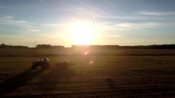 Tractor square baler silhouettes against tremendous sunset — Stock Video