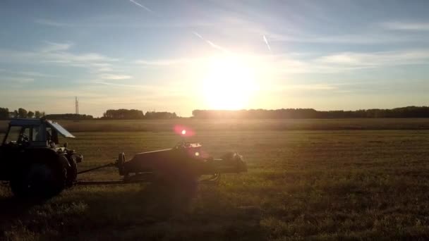 Traktor dengan baler persegi beroperasi di matahari terbenam cerah — Stok Video