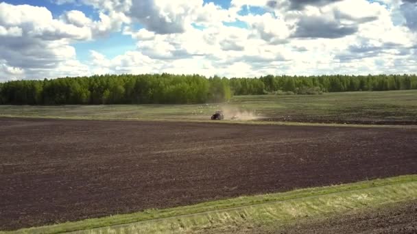 Aerial rörelse över plöjs fältet traktorn mot skogen — Stockvideo