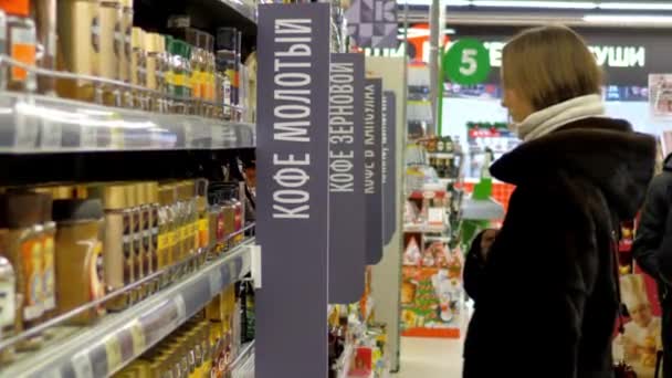 穿着毛皮大衣的年轻女子在超市里选择咖啡罐 — 图库视频影像