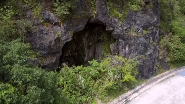 Zoom in rocky cave with lake by road curve among jungle — Stock Video