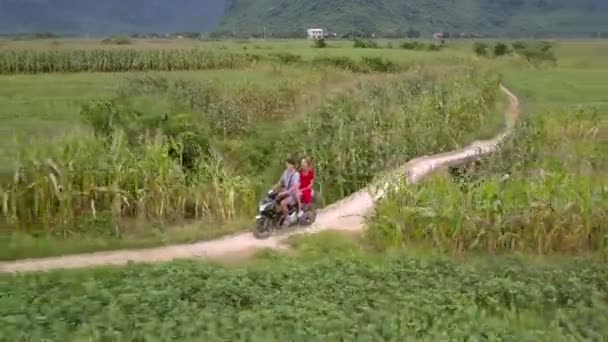 Hombre monta scooter con chica en el asiento trasero a lo largo de la carretera de tierra — Vídeos de Stock