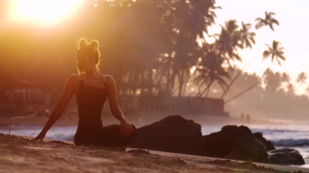 Kadın silueti, güneşin palmiyelerin arkasından doğuşunu meditasyon yapar. — Stok video