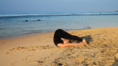 young beautiful woman lies on sandy beach in yoga pose