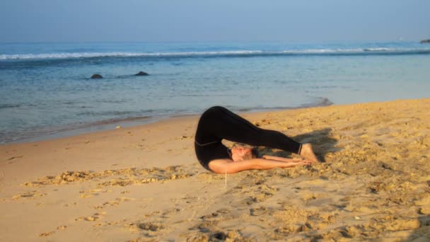 Jovem mulher bonita encontra-se na praia de areia em pose de ioga — Vídeo de Stock