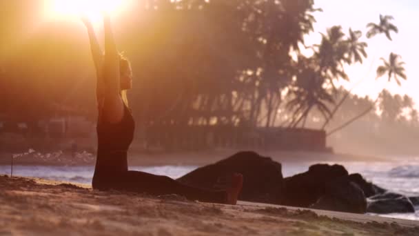 Tremendous lady practices yoga on sandy beach near stones — Stock Video