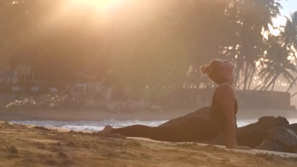 Jovem mulher alonga músculos fazendo ioga na praia no oceano — Vídeo de Stock