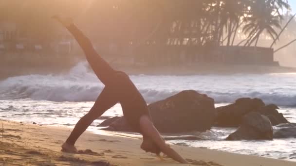 Young barefoot woman changes yoga pose on sandy beach — 비디오