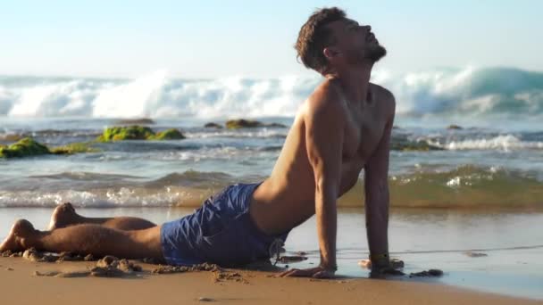 Handsome guy meditates in yoga pose on sandy beach — Stock Video