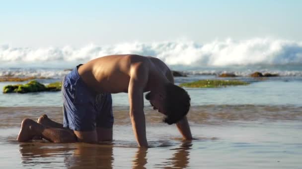 Muscular athlete stands on hands and knees in shallow water — Stock Video