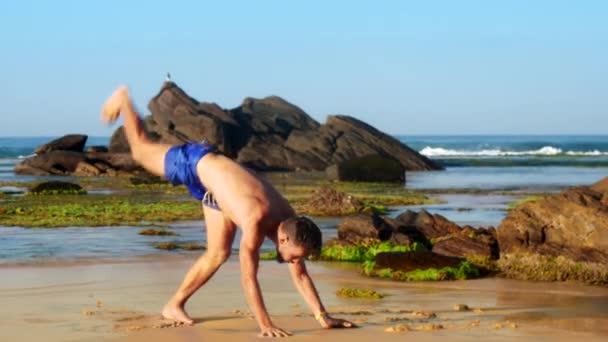 Stilig gymnast går på händer längs kustnära våt sand — Stockvideo