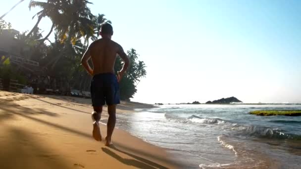 Mavi şort adam ıslak kum üzerinde ayak izleri bırakarak çalışır — Stok video