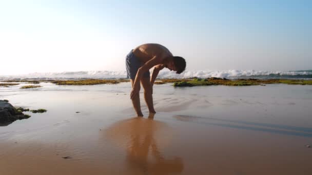 Muscoloso ragazzo in pantaloncini blu si estende indietro sulla spiaggia di sabbia — Video Stock