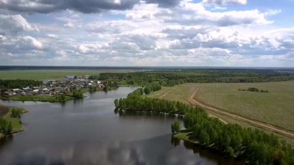 Malé vesnické střechy na klidném břehu řeky blízko nekonečných polí — Stock video