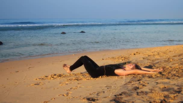 Belle dame en survêtement pratique l'exercice de yoga sur la plage — Video