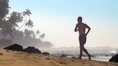 kaslı adam palmiye ağaçlarına karşı kumlu kıyı şeridi boyunca çalışır