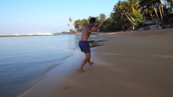 Muscular man in blue shorts exercises running along beach — Stock Video