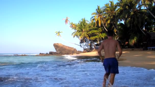 Ragazzo corre lungo onde oceaniche schiumose rotolando sulla spiaggia di sabbia — Video Stock