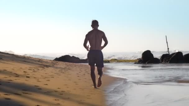 Atlet beyaz köpüklü okyanus dalgalarına karşı plaj boyunca çalışır — Stok video