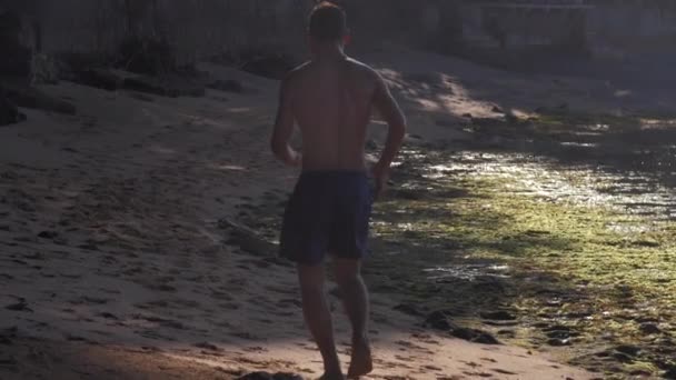 Gimnasta en pantalones cortos silueta corre a lo largo de la costa arenosa — Vídeos de Stock