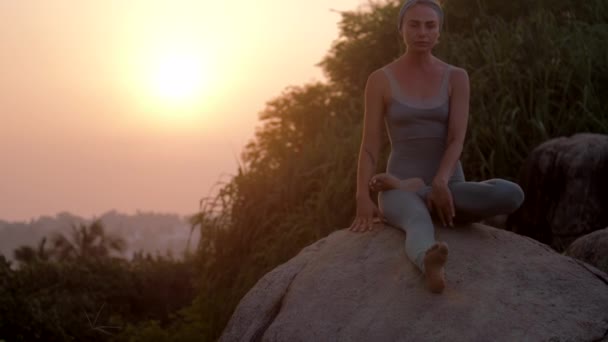 Femeie face fitness pe stâncă uriașă la răsăritul soarelui lent mișcare — Videoclip de stoc