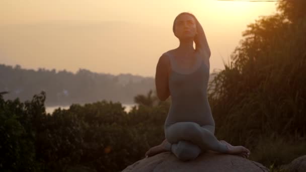 Yoga-Praktizierende sitzt in Gomukhasana auf Felsen-Zeitlupe — Stockvideo