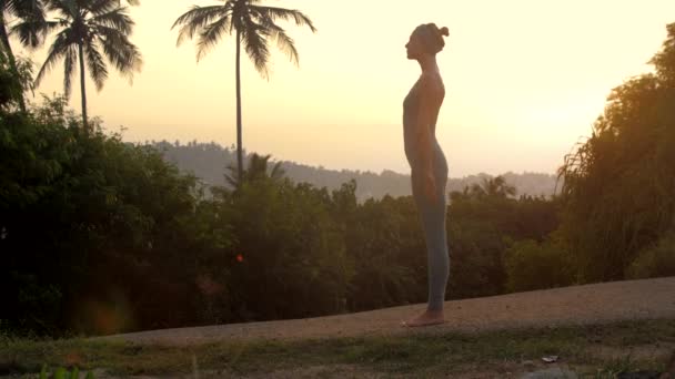 Mulher faz surya namaskara ioga perto de plantas câmera lenta — Vídeo de Stock